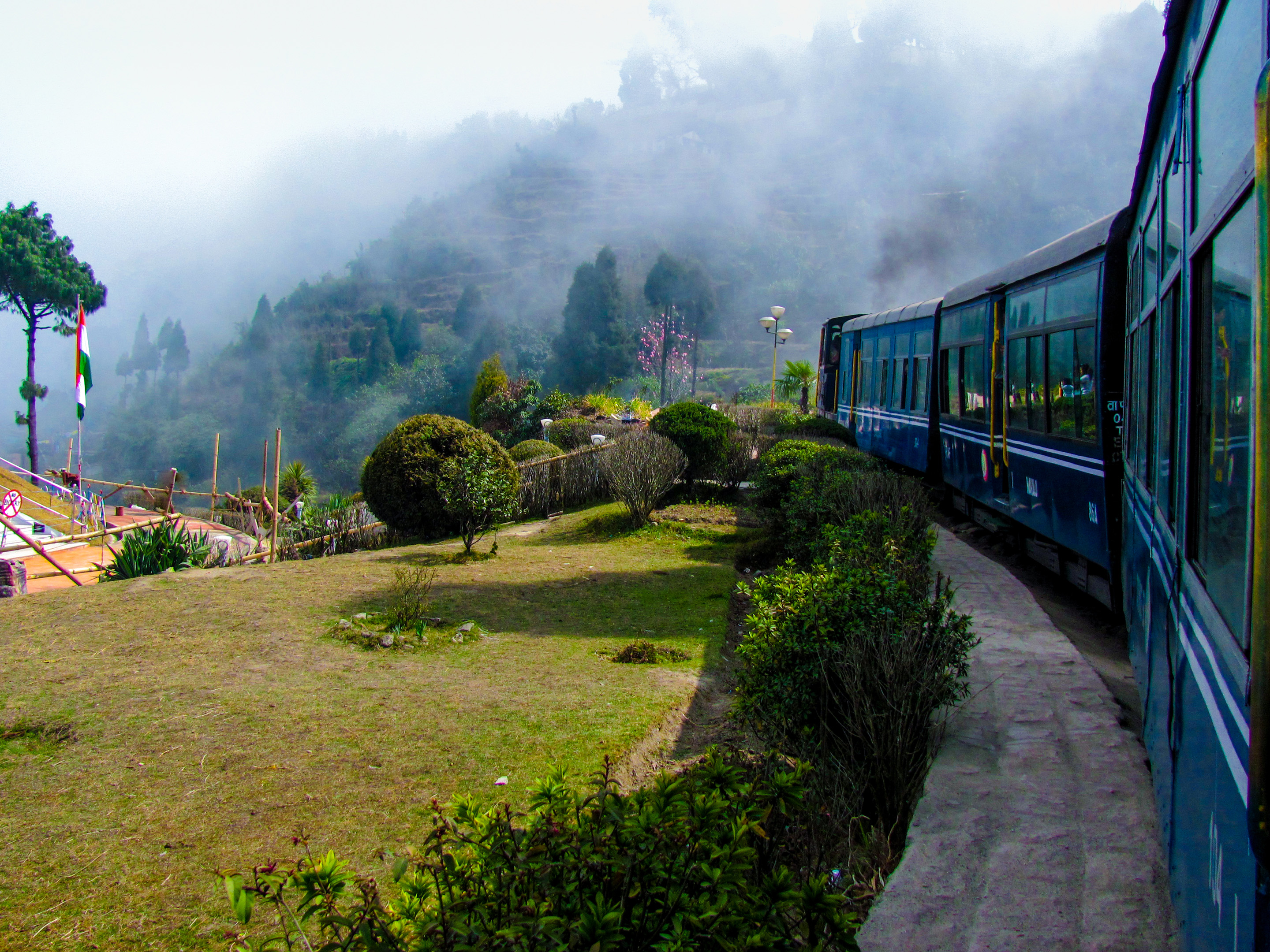 Train Passing A Beautiful Garden And Entering Into Fog. Surrounded By Tree Covered Mountains Shutterstock 184285343