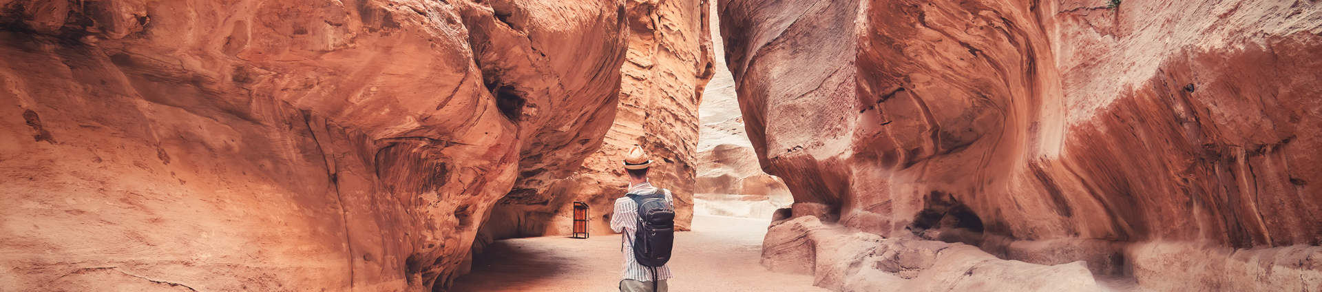 Tourist Walking Alone Through The Red Rock Walls Of The Main Road In The Ancient City Of Petra